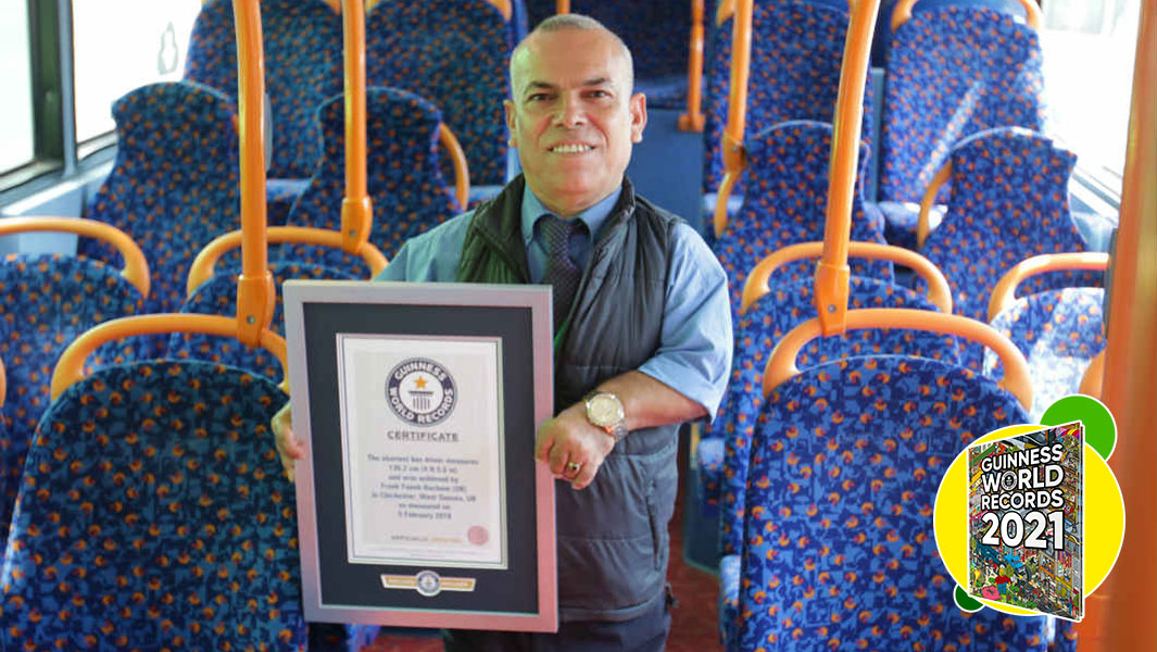 shortest bus driver standing in bus with 2021 book packshot